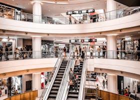 Modern shopping mall interior with vibrant atmosphere, featuring escalators and multiple levels of stores.